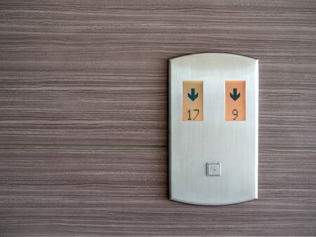 Digital number and down arrow on metallic elevator call panel on wooden pattern wall background with...