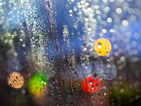 Blurred rain drops texture on car window with colorful bokeh abstract background.