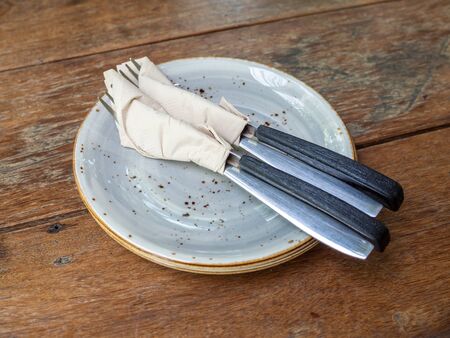 Two set of clean fork and knife wrapped in tissue napkin in the ceramic dish on wooden table.の写真素材