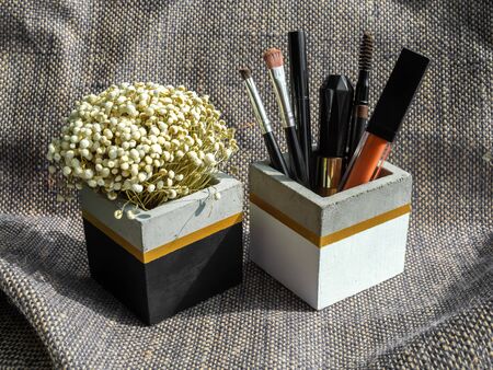 Cosmetic tools set and dried flower in cubic shape concrete container on sackcloth background.の写真素材