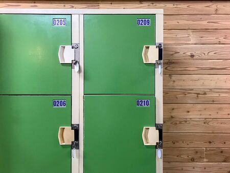 Old green locker cabinet with key on wooden wall background in locker room.の写真素材