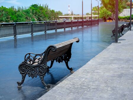 Empty old outdoor curved steel and wooden vintage bench on wide concrete terrace near steel fence and river.の写真素材