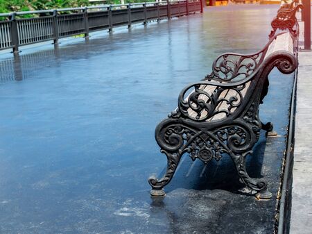 Empty old outdoor curved steel and wooden vintage bench on wide concrete terrace near steel fence and river.の写真素材
