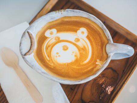 Close-up teddy bear latte art coffee in handmade ceramic cup on wooden tray on white background, top view.の写真素材