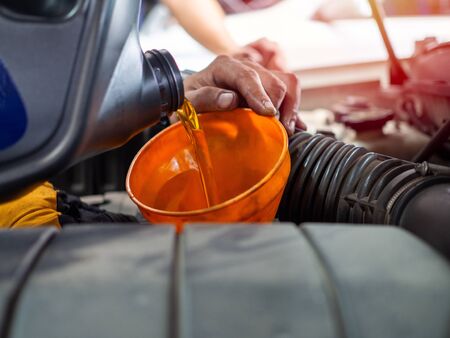 Mechanic hand pouring fresh  engine oil through orange funnel into the car engine at maintenance repair service station. Engine oil change.の写真素材