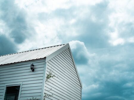 White wooden cabin against the cloud and blue sky background with copy space. Rain storm coming with dark clouds above white wooden house.の写真素材