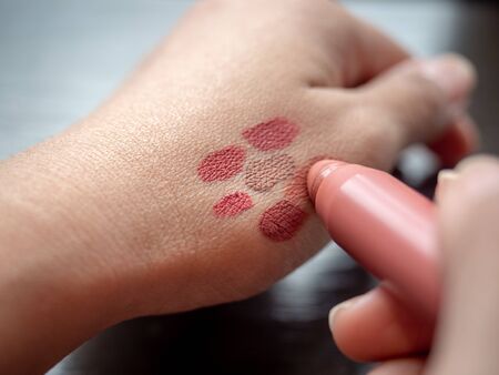 Close-up woman's hands testing colors of lipstick on skin.の写真素材