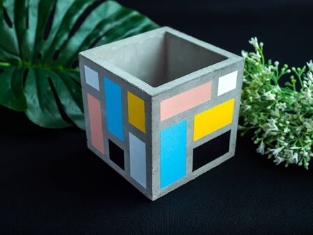 Cactus pot. Beautiful painted concrete pot. Empty modern cubic concrete planter with flowers and palm leaf on dark background.の写真素材