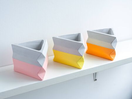 Cactus pot. Beautiful painted concrete pot. Three empty colorful modern triangle concrete planters, pink yellow and orange on white wooden shelf on white wall background.の写真素材