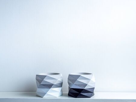 Cactus pot. Beautiful painted concrete pot. two empty modern geometric concrete planters, black and white painted on white wooden shelf on white wall background with copy space.の写真素材