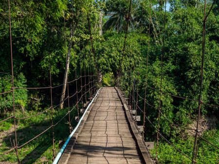 Hanging wooden bridge crossing to the rainforest. Empty suspension walkway bridge head to the other side, green tropical jungle.の写真素材