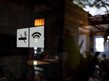 Signs on glass door. No smoking sign, wireless signal icon sign for free wifi on cafe background with copy space. Decal sticker signs pasted on front door outside the coffee shop.の写真素材