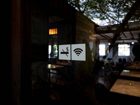 Signs on glass door. No smoking sign, wireless signal icon sign for free wifi on cafe background. Decal sticker signs pasted on front door outside the coffee shop.の写真素材