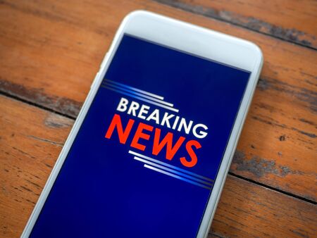 Close-up "Breaking news" online on screen  smartphone on wooden table with copy space, top view.の写真素材