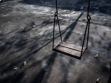 Old lonely wooden swing on sunset time with light and shadow. Vintage wood swing with leaves on the ground with copy space.の写真素材