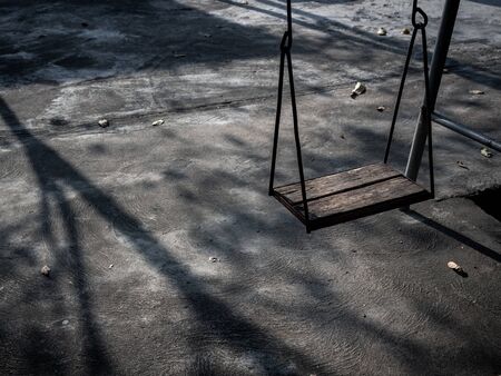 Old lonely wooden swing on sunset time with light and shadow. Vintage wood swing with leaves on the...