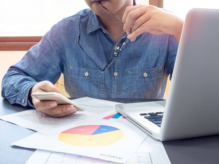 Asian businessman wearing blue shirt and holding glasses feel strain with working with laptop computer on table near the window in office.の写真素材