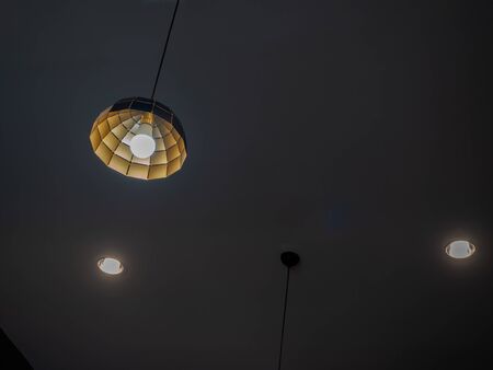 Modern ceiling light hanging from ceiling with downlight in dark room with copy space.の写真素材
