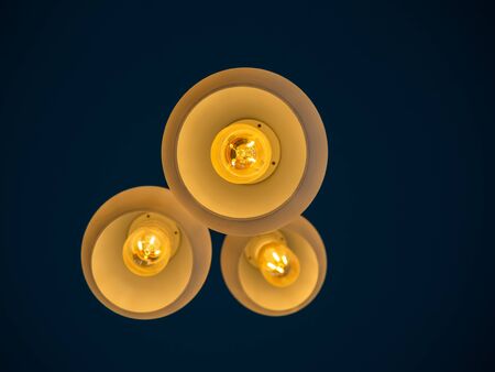 Three round modern ceiling lights hanging from ceiling from bottom view in dark blue room.の写真素材