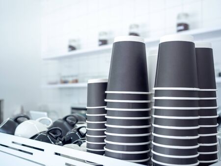 Black paper coffee cups stacked in a pile. Row of black paper cups upside down on shelf on white cafe background with copy space.の写真素材