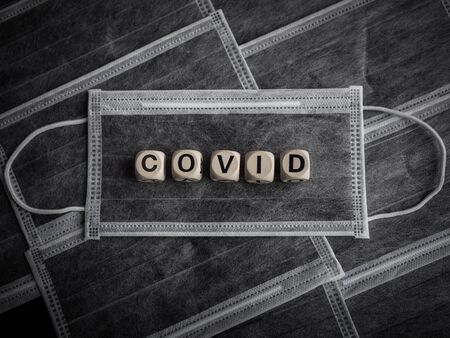 Coronavirus or Covid-19 concept. Wooden cubes text "COVID" on many protective face masks background.の写真素材