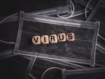 Coronavirus or Covid-19 concept. Wooden cubes text "VIRUS" on many protective face masks background.の写真素材
