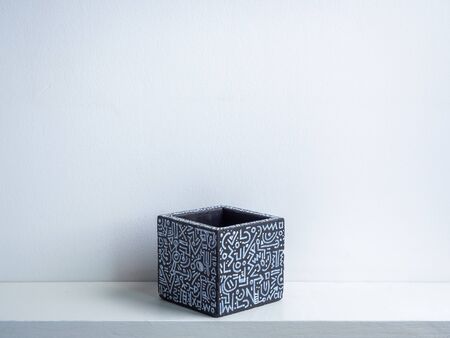 Cactus pot. Concrete pot. Empty black with modern graphic pattern geometric concrete planter on white wooden shelf isolated on white wall background.の写真素材