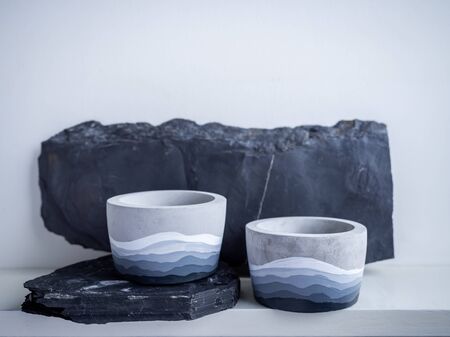 Cactus pot. Concrete pot. Two empty modern geometric concrete planters with painted on rock on white wooden shelf isolated on white wall background.の写真素材