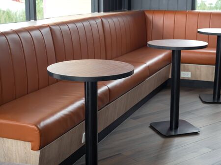 Furniture decoration in cafe retro style. Empty round wood table bars and orange long leather sofa on wood floor with natural daylight.の写真素材