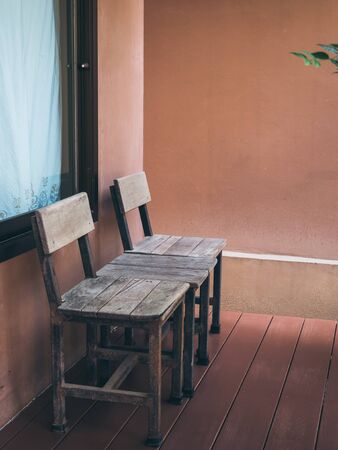 Old twin wooden chair on wooden terrace in front of room with glass window. Stay at home with relaxation concept, vertical style.の写真素材