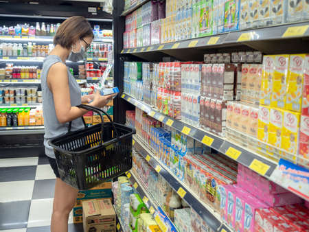 Bangkok, Thailand - April 14, 2020: Asian woman wearing protective face mask holding shopping basket and choosing milk product in supermarket in Bangkok, Thailand.のeditorial素材