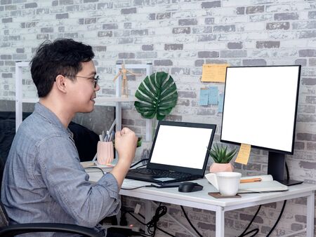 Asian man with success hand working with laptop computer with white blank screen and watching another monitor in his room, condominium. Work at home and business online concept.の写真素材
