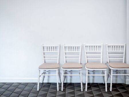 Row of clean white vintage wooden chairs with pads on modern stone tiles floor on white wall background with copy space.の写真素材