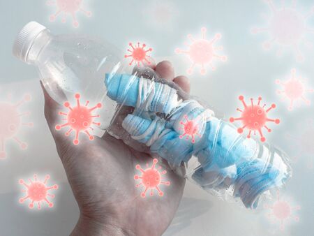 Used mask concept. Hand holding plastic bottle with folded used protective face mask inside it with...