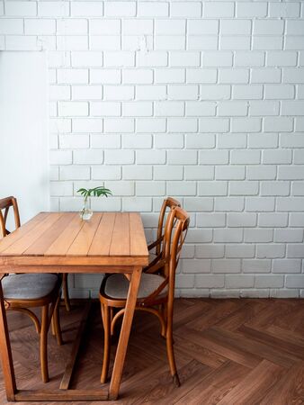 Wooden dining table and four chairs with green leaf in glass vase on white wall background in restaurant with copy space, vertical style.の写真素材