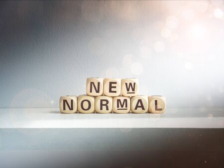Beautiful bokeh from sunlight shines on New Normal, words on wooden alphabet cube on dark background. New normal after covid-19 pandemic concept.の写真素材