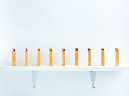 New normal and social distancing concept. New Normal, words on wooden alphabet cube on row of wooden dominoes with distance space on shelf on white background.の写真素材