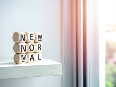 Close-up New Normal, words on wooden alphabet cube on shelf near window with sunlight. New normal after covid-19 pandemic concept.の写真素材