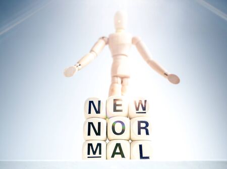 New Normal, words on wooden alphabet cube and wooden figure on white background with sparkle light. New normal life after covid-19 pandemic concept.の写真素材