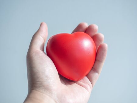 Red heart. Close-up big red heart ball in hand on grey background.の写真素材