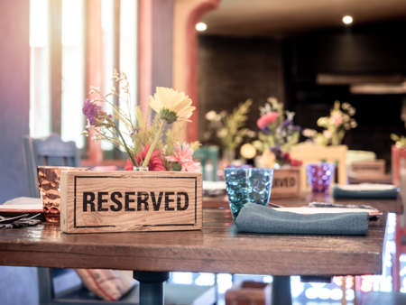 Wooden reserved sign standing with glass and flower pot on dining table in retro style restaurant.
