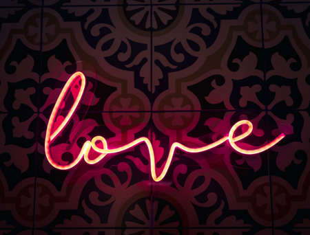 Love. Neon sign letter word Love in bright red colours glow in the dark on pattern tiles wall background.の写真素材
