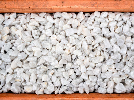 White pebble background. Stone gravel texture in terracotta pot, top view.