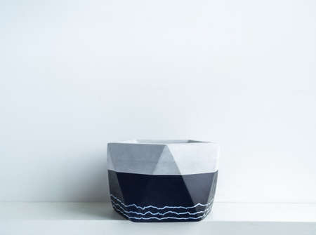 Empty modern geometric concrete planter on white shelf isolated on white wall background with copy space. Beautiful black colour painted cement pot.の写真素材