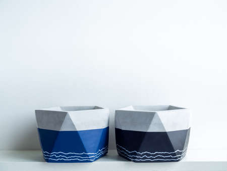 Empty modern geometric concrete planters on white shelf isolated on white wall background with copy space. Two beautiful blue and black colour painted cement pots.の写真素材