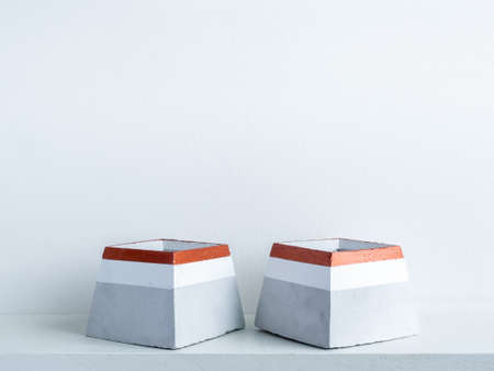 Two empty modern geometric concrete planters decoration on white shelf isolated on white wall background with copy space. Beautiful painted pyramid shaped cement pots.の写真素材