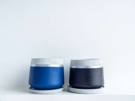 Two empty modern geometric concrete planters on white shelf isolated on white wall background with copy space. Beautiful blue and black colour painted cement pot.の写真素材
