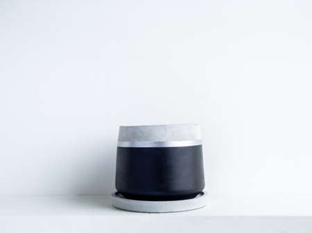 Empty modern geometric concrete planter on white shelf isolated on white wall background with copy space. Beautiful black and silver colour painted cement pot.の写真素材