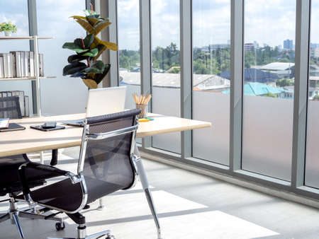 Modern office interior with huge windows with blue sky view. Wooden desk in corner of contemporary...