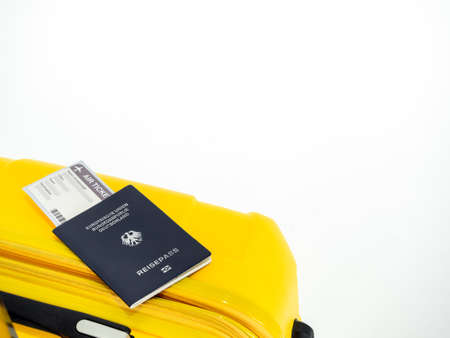 Passport and airline boarding pass ticket on yellow suitcase isolated on white background with copy space. Blue passport of Germany on yellow luggage, travel concept.のeditorial素材